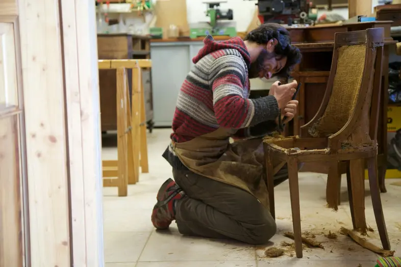 Man repairing wooden chair in workshop.